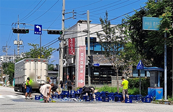 ▲江原道春川市東面の万泉路を走行していたトラックから大量のビールが落下した。写真は後片付けをする周辺住民。12日午前撮影。／聯合ニュース