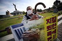 ▲ソウル市鍾路区の青瓦台噴水台前で21日午前、江原道鉄原郡二吉里の住民が「家の中に地雷爆弾」と書かれたプラカードを持ち、集団移住対策の整備を訴えるデモを行っているところ。／写真＝聯合ニュース