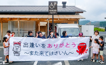 ▲「出逢（あ）いをありがとう、また来てけさいん」と宮城の方言で書かれた横断幕を持って韓国人学生たちを見送っているホームステイの家族たち。／キム・フィウォン記者