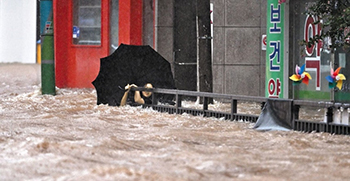 ▲17日、光州広域市に降った豪雨で、北区庁前の道路が浸水した。写真は水に流されないように橋の欄干につかまり、救助を求める人。光州市内には同日だけで午後10時までに412.7ミリメートルの雨が降った。写真＝NEWSIS